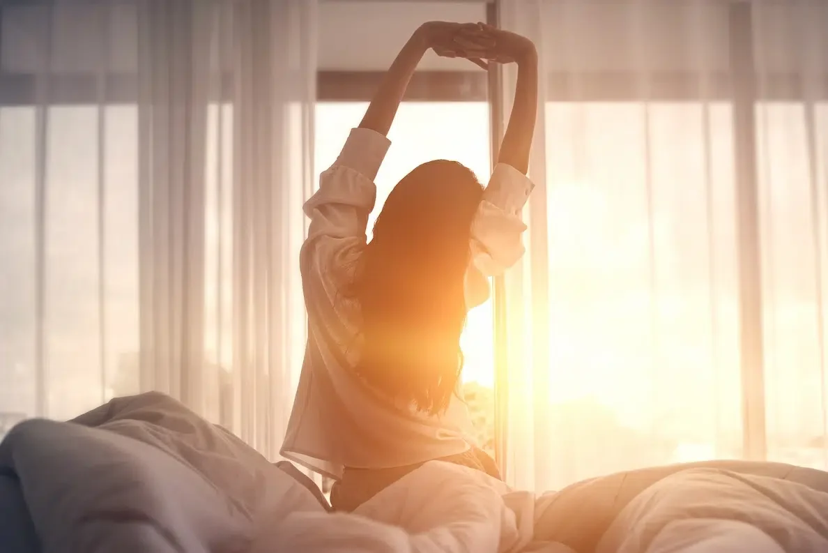 Eine Frau sitzt im Bett und streckt sich vor einem atemberaubenden Sonnenaufgang
