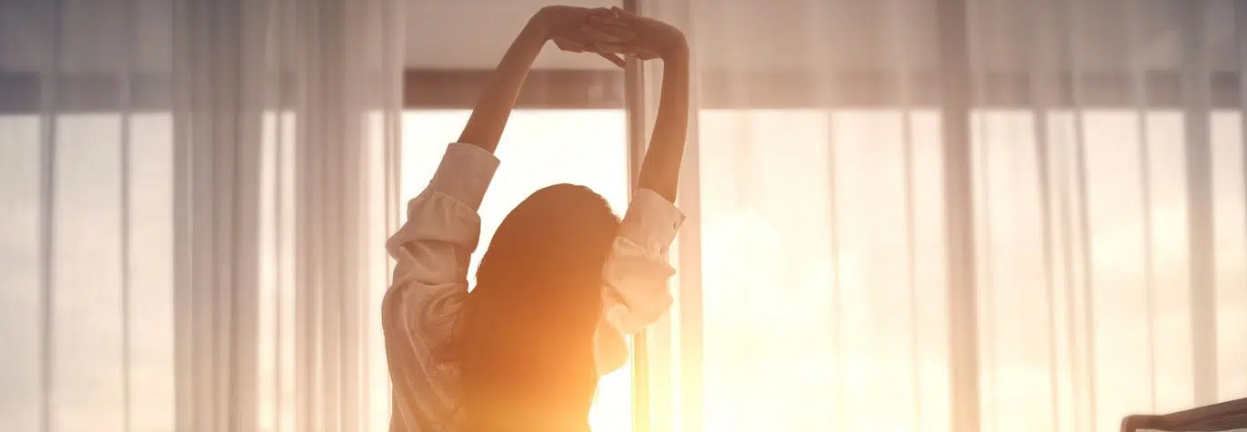 Eine Frau dehnt sich vor dem Fenster bei Sonnenaufgang