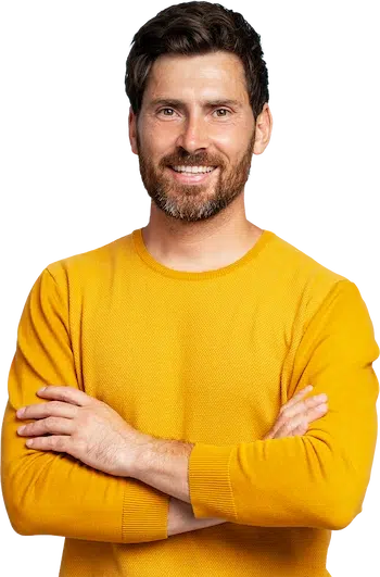 Mann in einem gelben Pulli mit verschränkten Armen lächelt