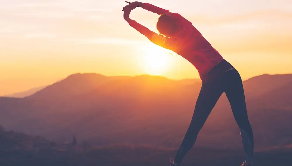 Eine Frau dehnt sich vor malerischem Sonnenaufgang